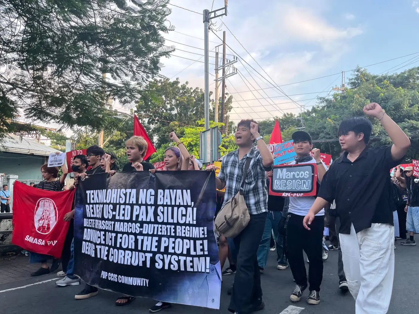 Students marching with a black banner reading Teknolohista ng Bayan, reject US-led Pax Silica, advance ICT for the people, debug the corrupt system