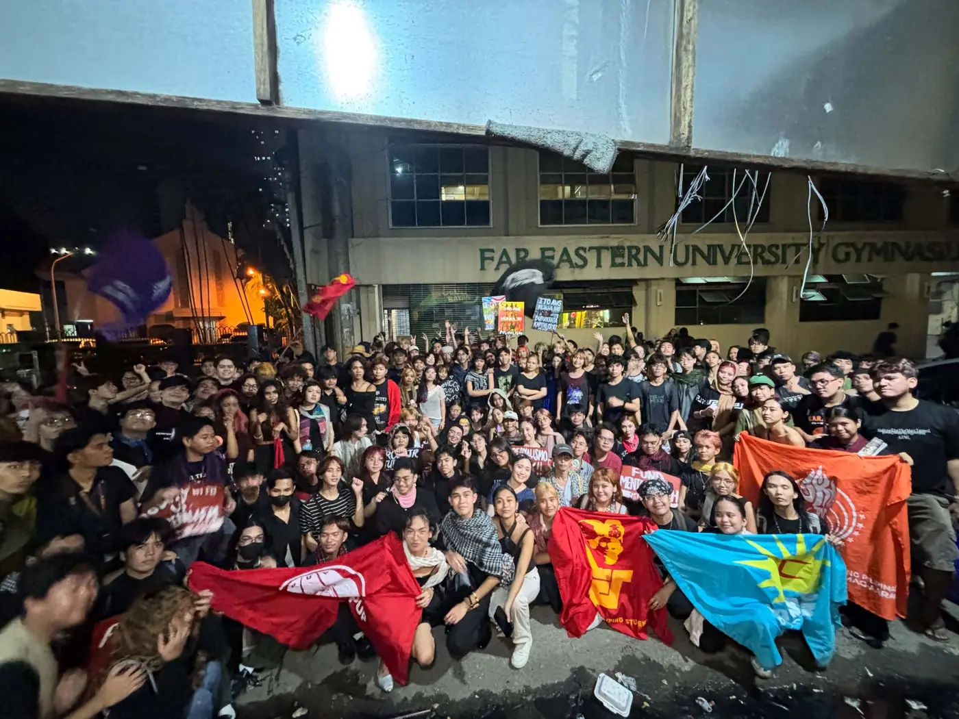 Hundreds of students posing together with flags at night in front of the Far Eastern University Gymnasium after the march